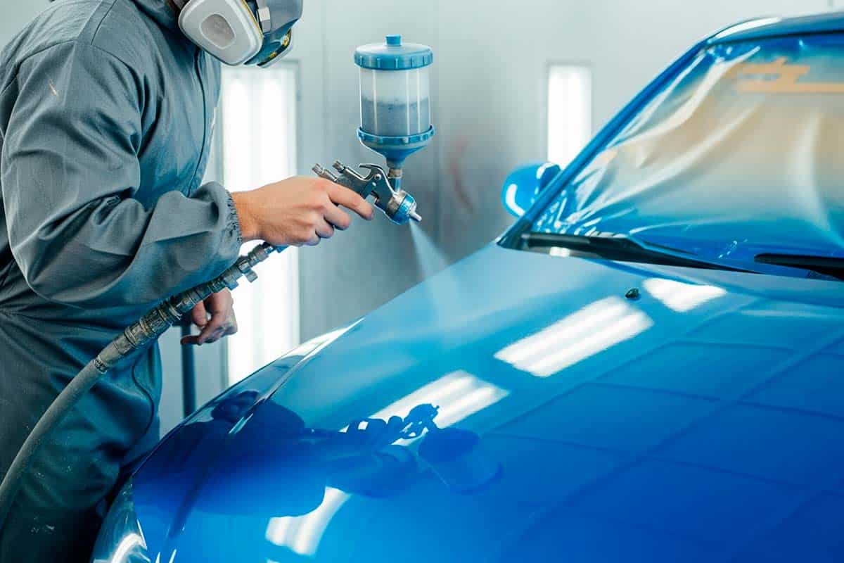 Foto de um mecânico pintando um carro.