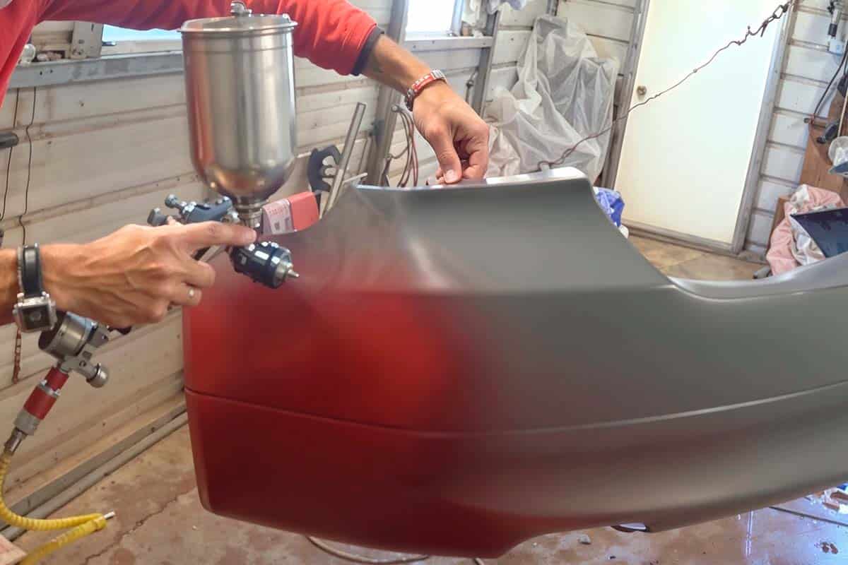 Foto de um mecânico pintando o para-choque de um carro.